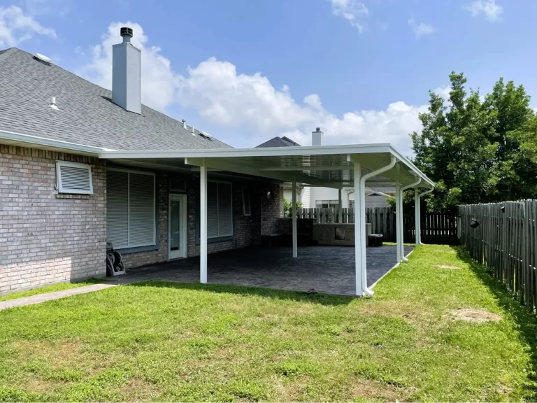 Covered patio with a white roof providing shade and shelter in a Southeast Louisiana backyard, featuring a brick house, green lawn, and blue sky.