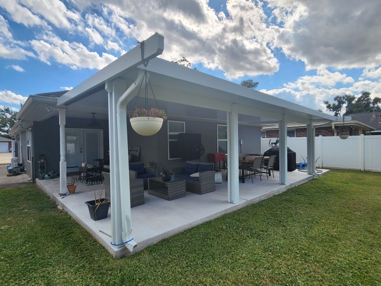 Aluminum patio cover installed over a backyard concrete patio at a New Orleans area home, creating shaded seating and outdoor dining space beside the house.