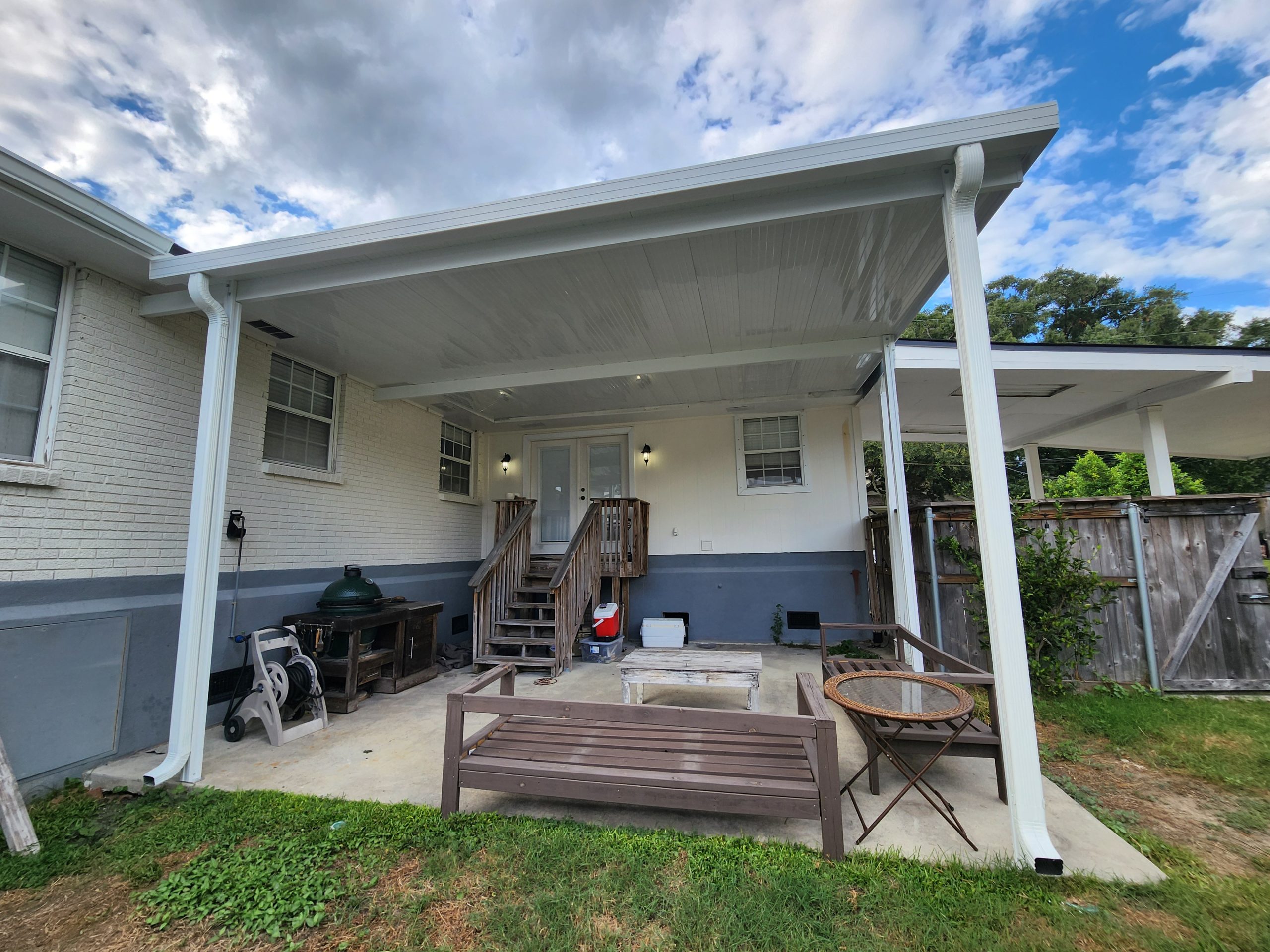 White aluminum patio cover attached to a Louisiana home, creating shaded outdoor seating space over a concrete patio in a residential backyard.